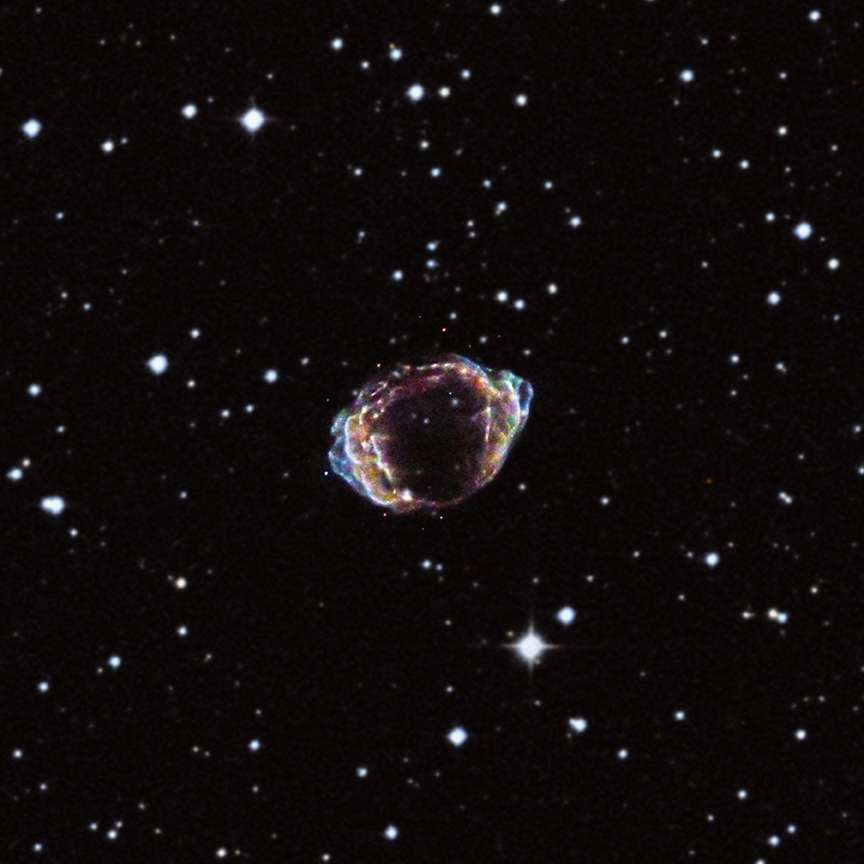 Image composite dans les rayonnements visible et X du reste de supernova G1.9+0.3 et ses environs, publiée en 2013. Si l’on retranche les observations réalisées avec le télescope spatial Chandra, on devient comme aveugle, ne distinguant que les quelques étoiles au premier plan et rien des nuages de débris, bien cachés derrière un épais voile de poussière. © Nasa, CXC, NCSU, DSS