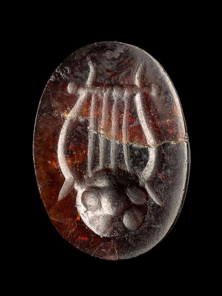 La gema roja grabada con una lira es más pequeña que una falange y es uno de los muchos restos encontrados con naufragios.  © Yaniv Berman, Autoridad de Antigüedades de Israel