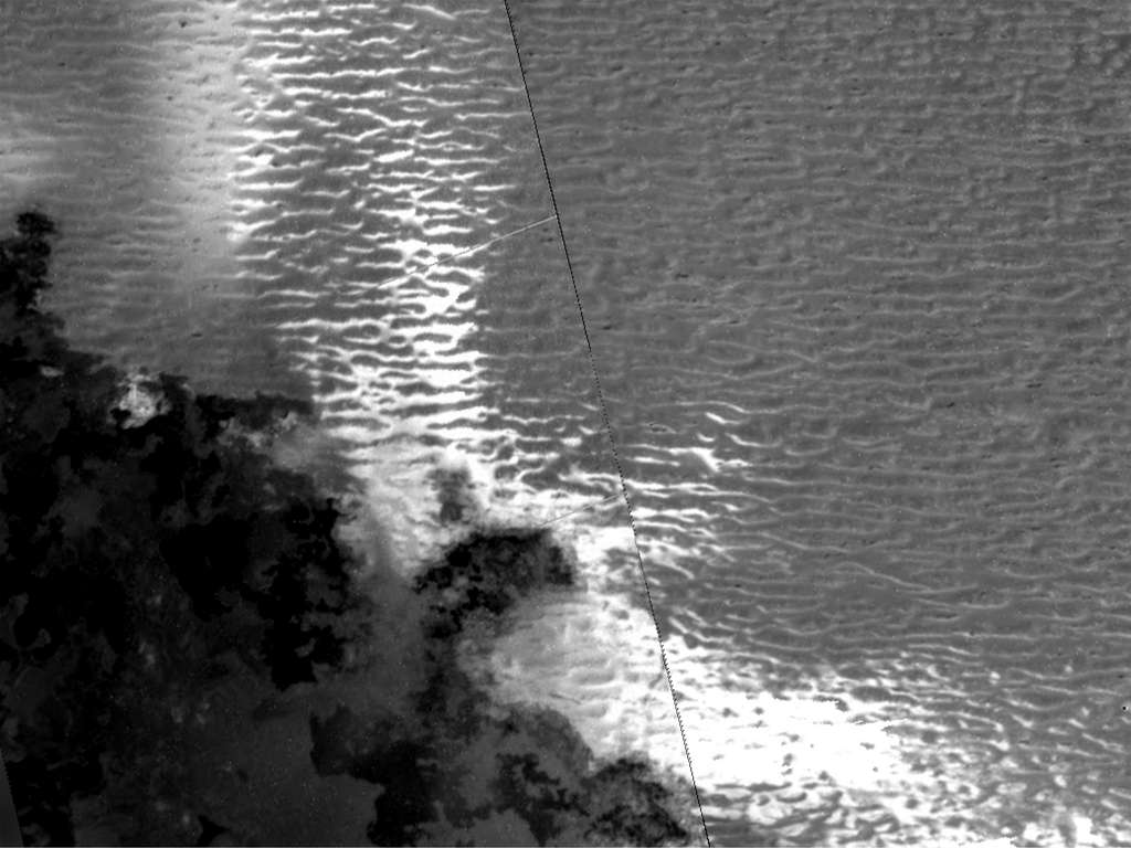 Dunes potentielles sur Io, la lune de Jupiter. Une analyse indique que le matériau sombre (en bas à gauche) est formé de coulées de lave récemment mises en place, tandis que les caractéristiques répétées en forme de ligne dominant l'image sont des dunes potentielles. Les zones blanches et brillantes peuvent être des grains nouvellement mis en place lorsque les coulées de lave vaporisent le givre de dioxyde de soufre adjacent. © Nasa, JPL-Caltech, Rutgers