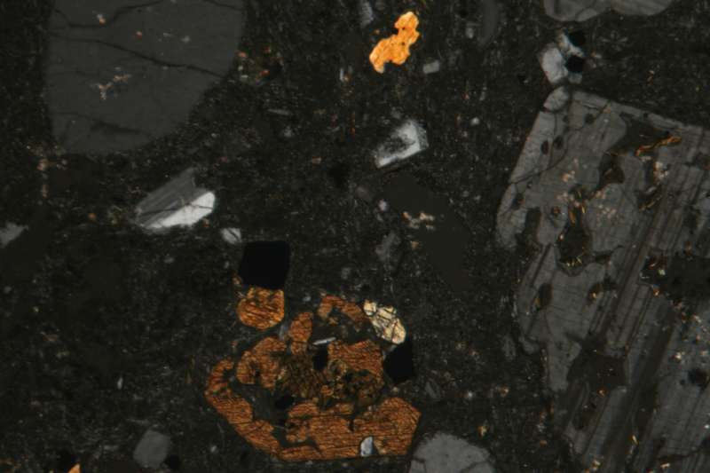 Lame mince d’andésite observée au microscope à lumière polarisée-analysée. Les phénocristaux de feldspaths plagioclases (gris) et d’amphiboles (marron) sont noyés dans une pâte microlitique (noire) © Siim, Wikimedia Commons, CC by-sa 3.0