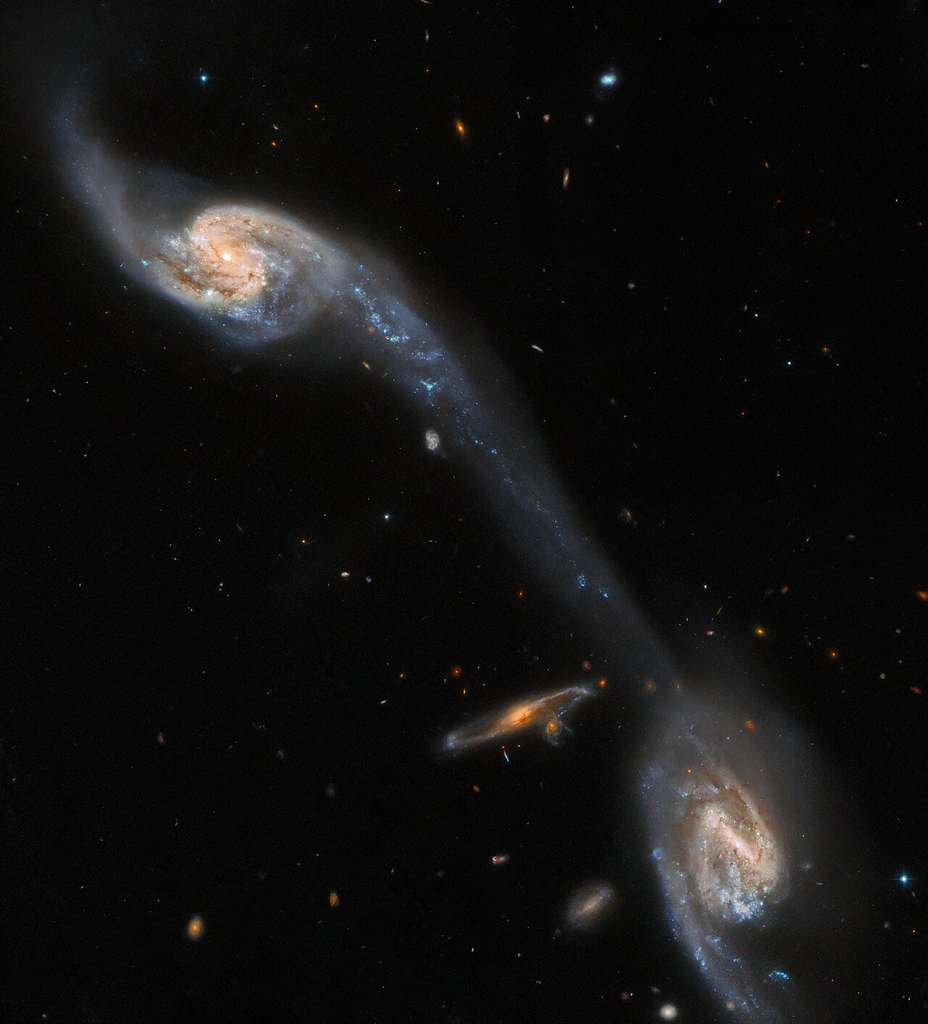 Cette image du télescope spatial Hubble montre deux des galaxies du triplet galactique Arp 248 – également connu sous le nom de triplet de Wild – qui se trouve à environ 200 millions d'années-lumière de la Terre dans la constellation de la Vierge. Les deux grandes galaxies spirales visibles sur cette image – qui flanquent une galaxie spirale d’arrière-plan plus petite et sans rapport – semblent être reliées par un pont lumineux. Ce flux allongé d’étoiles et de poussière interstellaire est connu sous le nom de queue de marée et il a été formé par l’attraction gravitationnelle mutuelle des deux galaxies du premier plan. Cette observation vient du catalogue des galaxies et associations particulières du sud, compilé par les astronomes Halton Arp et Barry Madore, et de l’Atlas des galaxies particulières, compilé par Halton Arp. © ESA/Hubble & Nasa, Dark Energy Survey/DOE/FNAL/DECam/CTIO/NOIRLab/NSF/AURA, J. Dalcanto