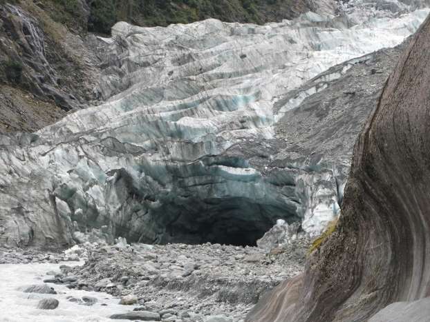 Terminaison du glacier Franz Josef montrant le ruisseau sous-glaciaire dont les eaux sont chargées de particules sédimentaires. Les roches affleurant sur la droite ont été fortement érodées par l’abrasion du glacier avant son retrait. © O. Beyssac
