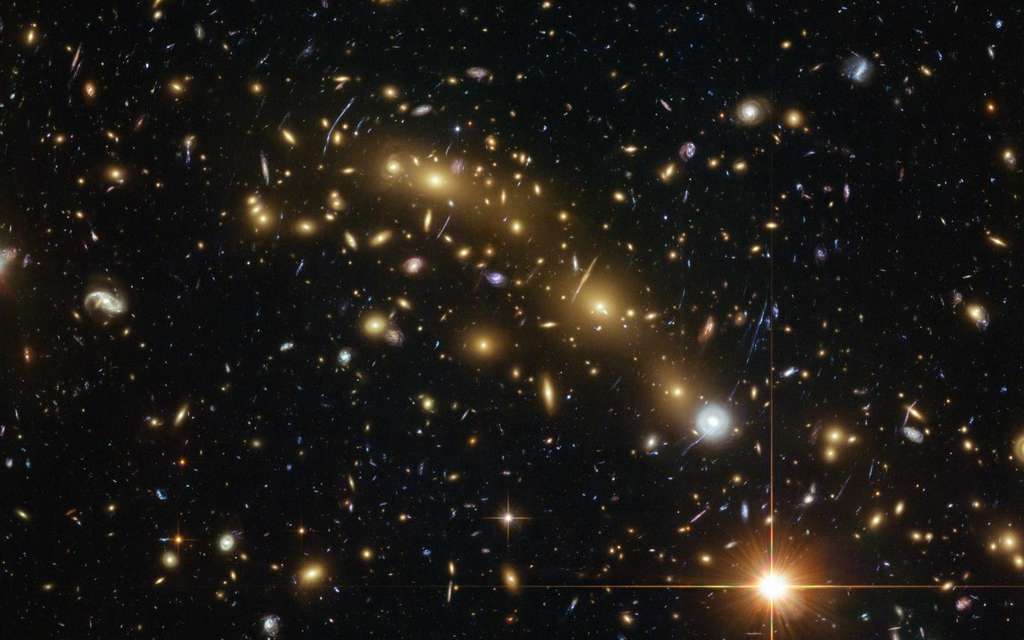 Image en couleur de l'amas de galaxies utilisé pour détecter et étudier par effet de lentille gravitationnelle l'une des six plus vieilles galaxies connues, MACS0416-JD. Cette galaxie a un âge estimé à 351 millions d'années, ce qui signifie que sa formation a débuté 178 millions d'années après le Big Bang. La masse stellaire de cette galaxie est un milliard de fois la masse du Soleil. Cet objet est actuellement en fait la galaxie la plus éloignée détectée avec Alma. © ESA/Hubble, Nasa, HST Frontier Fields