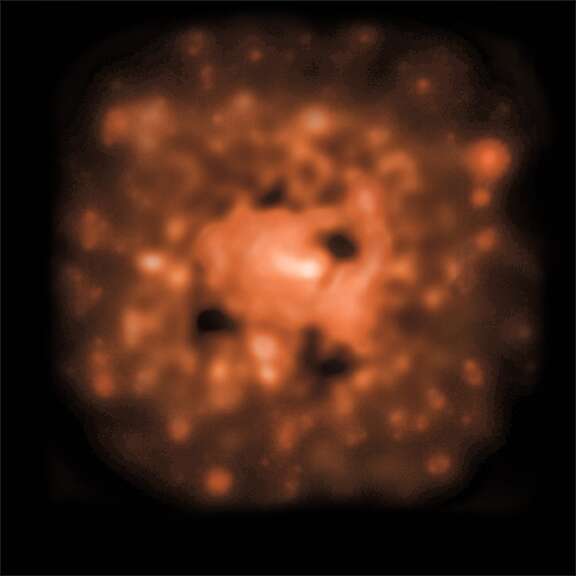 Des observations dans le domaine des rayons X par Chandra de 4C +00.58 montrent une vaste zone emplie de gaz chauds mais avec 4 cavités. Ce sont les quatre taches sombres sur cette image. Crédits : rayon x : NASA CXC UMD Hodges-Kluck et al. ) ; radio : NSF NRAO VLA UMD Hodges-Kluck et al. ; SDSS