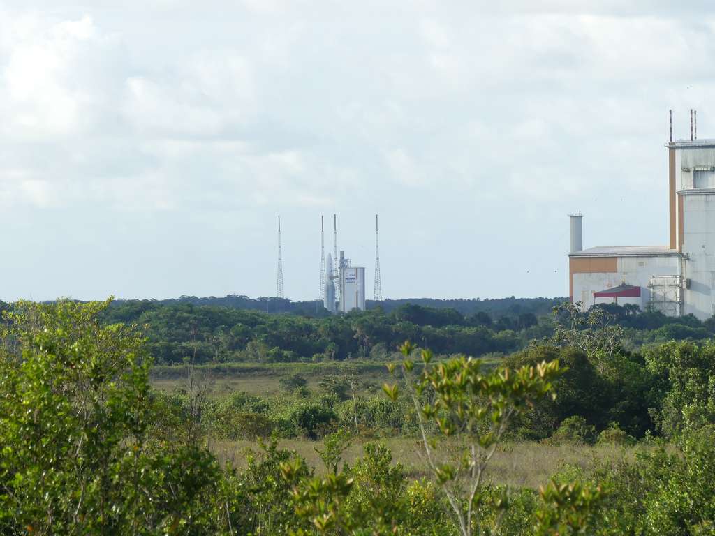 Quelques minutes avant le décollage, Ariane 5 attend. La fumée blanche qui s'échappe montre que les réservoirs d'ergols liquides sont bien sous pression. D'ailleurs le remplissage dure jusqu'à quelques minutes avant l'envol. À droite, le BAF, d'où est roulée Ariane 5 jusqu'au pas de tir à J-1. © Daniel Chrétien, Futura Sciences