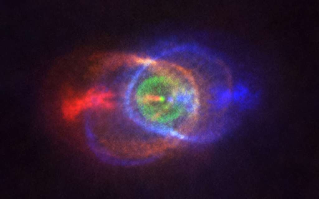 Cette nouvelle image acquise par Alma témoigne de l’issue d’un combat stellaire : une structure de gaz complexe et étonnante en périphérie du système binaire HD101584. Les couleurs représentent la vitesse, s’échelonnant du bleu – le gaz se déplaçant le plus rapidement dans notre direction – au rouge – le gaz s’éloignant le plus rapidement dans la direction opposée. Les jets situés le long de la ligne de visée propulsent la matière figurée en bleu ou rouge. Les étoiles de la binaire forment un seul et unique point brillant au sein de la structure annulaire colorée en vert, qui se déplace à la même vitesse que l’ensemble du système le long de la ligne de visée. Aux dires des astronomes, cet anneau trouve son origine dans la matière éjectée, alors que l’étoile de masse inférieure spiralait en direction de son compagnon, la géante rouge. © Alma (ESO/NAOJ/NRAO), Olofsson et al. Remerciements : Robert Cumming