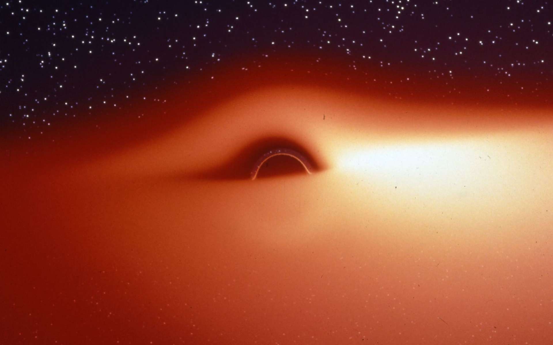 Le champ de gravitation d'un trou noir déforme fortement l'image du disque d'accrétion qui l'entoure et qui contient un plasma chaud et lumineux en rotation autour de l'astre. On peut s'en rendre compte avec cette image, extraite d'une simulation de ce que verrait un observateur s'approchant de l'astre compact selon une direction légèrement inclinée au-dessus du disque d'accrétion. La partie du disque située derrière le trou noir semble tordue à 90° et devient visible au-dessus du trou noir. Du fait du décalage Doppler, le disque d'accrétion est plus lumineux d'un côté que de l'autre. Jean-Pierre Luminet a fait la première simulation de ces images en 1979, bien avant celle montrée dans Interstellar qui contient, fiction oblige, quelques simplifications trompeuses. © Jean-Pierre Luminet, Jean-Alain Marck