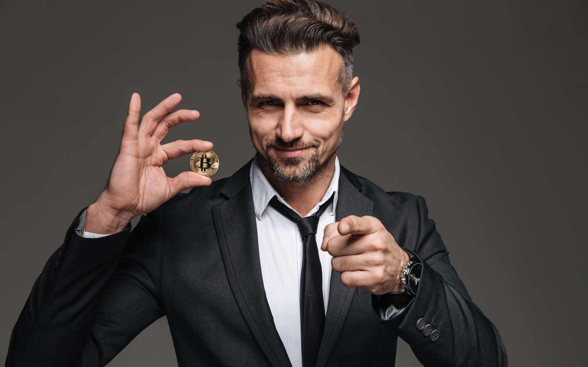 L'image d'un entrepreneur en costume et cravate qui tient un Bitcoin dans la main. © Drobot Dean