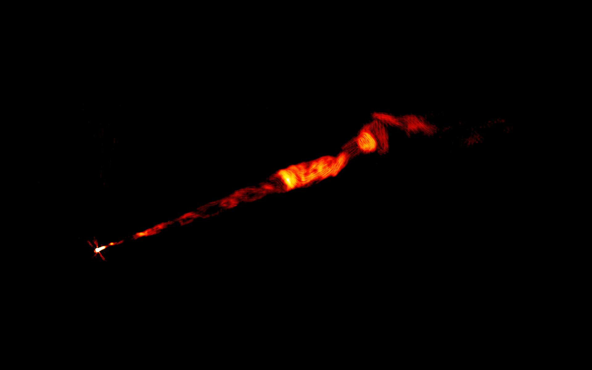 Cette image en fausses couleurs du VLA, réalisée à plusieurs fréquences radio, montre un jet dans le domaine radio provenant de la galaxie M87. Le jet, vu sur cette image, mesure environ 8.000 années-lumière. Cette image montre clairement la structure hélicoïdale en forme de tire-bouchon dans la partie interne du jet, qui prend naissance au point lumineux à gauche, au cœur de la galaxie, où réside un trou noir supermassif. © Pasetto et al., Sophia Dagnello, NRAO/AUI/NSF