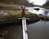 Image générée par intelligence artificielle d'une épée de style viking sur les rives d'un cours d'eau. © OpenArt.ai