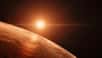 Nous voici près de Trappist-1 h, la plus éloignée des sept planètes de tailles terrestres qui gravitent autour de Trappist-1. Son petit soleil rougeoyant est à moins de 10 millions de kilomètres, soit un sixième de la distance entre Mercure et le Soleil. Depuis ce monde qui, selon la composition de son atmosphère peut être couvert d’eau liquide ou de glace, on peut voir ses six sœurs transiter devant leur étoile.
