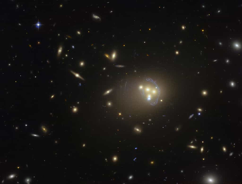 Cette image acquise par le télescope spatial Hubble du consortium Nasa-Esa montre le riche amas galactique Abell 3827. Les étranges structures de couleur bleue qui entourent les galaxies centrales constituent des vues agrandies, par effet de lentille gravitationnelle, d'une galaxie plus lointaine située derrière l'amas. Des observations de la fusion des quatre galaxies centrales ont démontré que la matière noire entourant l'une des galaxies ne suit pas le mouvement de la galaxie elle-même. Ce résultat permet d'envisager l'existence d'interactions matière noire – matière noire de nature inconnue. © ESO