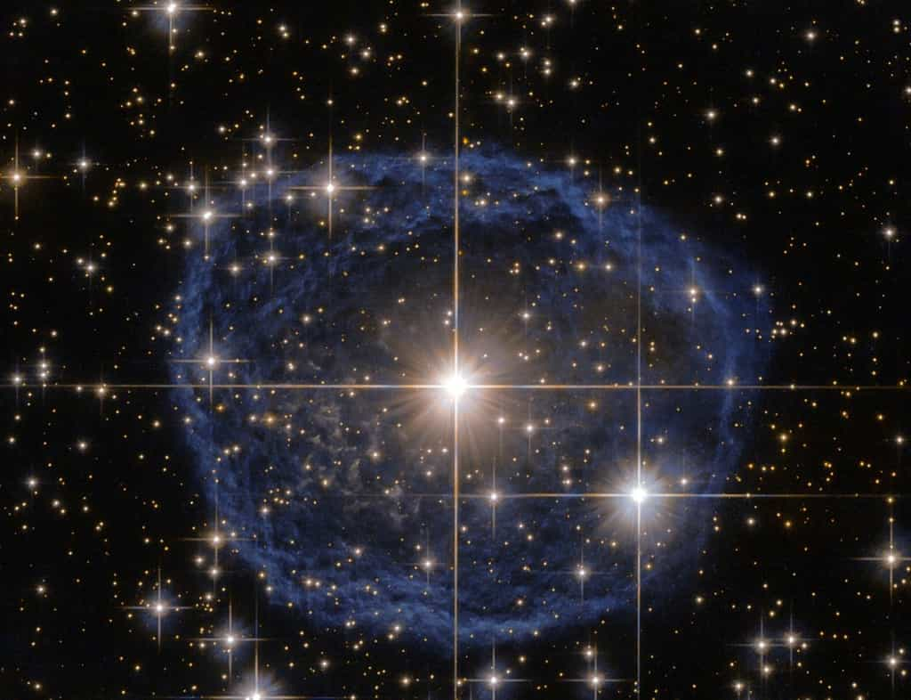 Une grande bulle bleue avec une étoile brillante au centre sur un fond noir rempli d'étoiles, c'est une belle image du télescope spatial Hubble de la Nasa/ESA qui montre une étoile Wolf-Rayet connue sous le nom de WR 31a, située à environ 30 000 années-lumière de la Terre dans la constellation de la Carène (La Quille). La bulle bleue caractéristique qui semble encercler WR 31a est une nébuleuse Wolf-Rayet, un nuage interstellaire de poussière, d'hydrogène, d'hélium et d'autres gaz. Créées lorsque des vents stellaires rapides interagissent avec les couches externes d'hydrogène éjectées par les étoiles Wolf-Rayet, ces nébuleuses sont souvent en forme d'anneau ou sphériques. La bulle, dont la formation remonte à environ 20 000 ans, se dilate à une vitesse d'environ 220 000 kilomètres par heure ! Malheureusement, le cycle de vie d'une étoile Wolf-Rayet n'est que de quelques centaines de milliers d'années, soit un clin d'œil en matière cosmique. Bien que leur vie ait débuté avec une masse au moins 20 fois supérieure à celle du Soleil, les étoiles Wolf-Rayet perdent généralement la moitié de leur masse en moins de 100 000 ans. Et WR 31a ne fait pas exception à la règle. Elle finira donc sa vie en une supernova spectaculaire, et la matière stellaire expulsée par son explosion nourrira plus tard une nouvelle génération d'étoiles et de planètes. © ESA/Hubble &amp; Nasa, Remerciements : Judy Schmidt