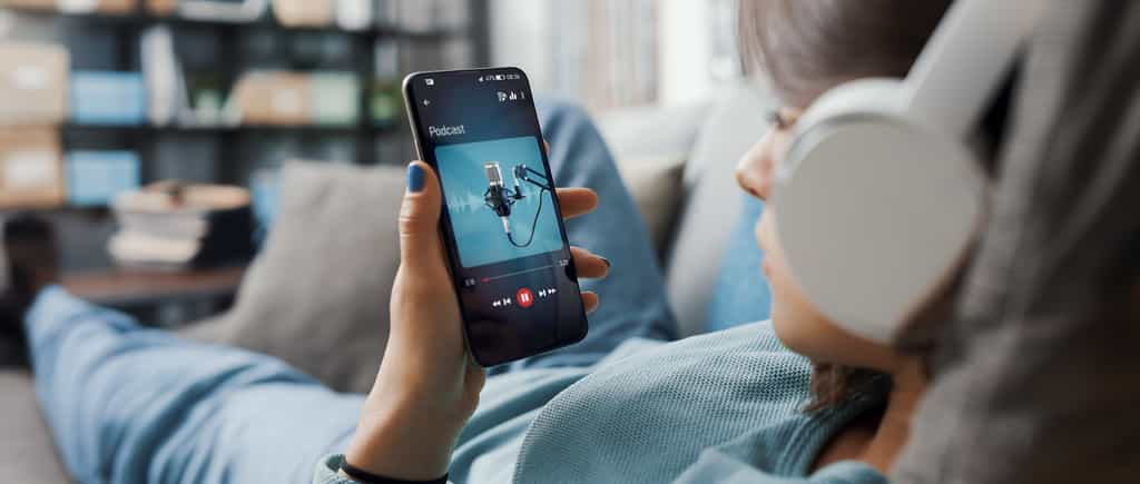 Une jeune personne écoute un podcast, allongée sur son canapé. © Adobe Stock, StockPhotoPro, image étendue grâce à l'IA   