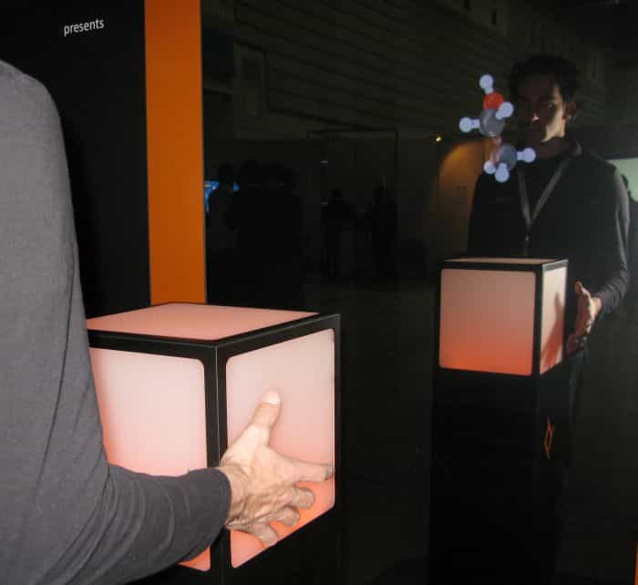 Debout devant le Cubtile, l'homme manipule à l'aide de ses deux mains, en effleurant les surfaces tactiles, l'objet apparaissant devant lui sur le miroir-écran. © Nikkei Electronics