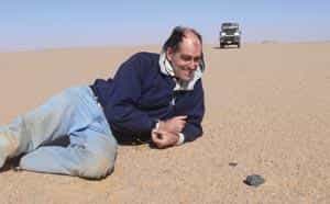 Peter Jenniskens pose devant un morceau de 2008 TC3, bien noir sur le sable du Sahara. © Peter Jenniskens