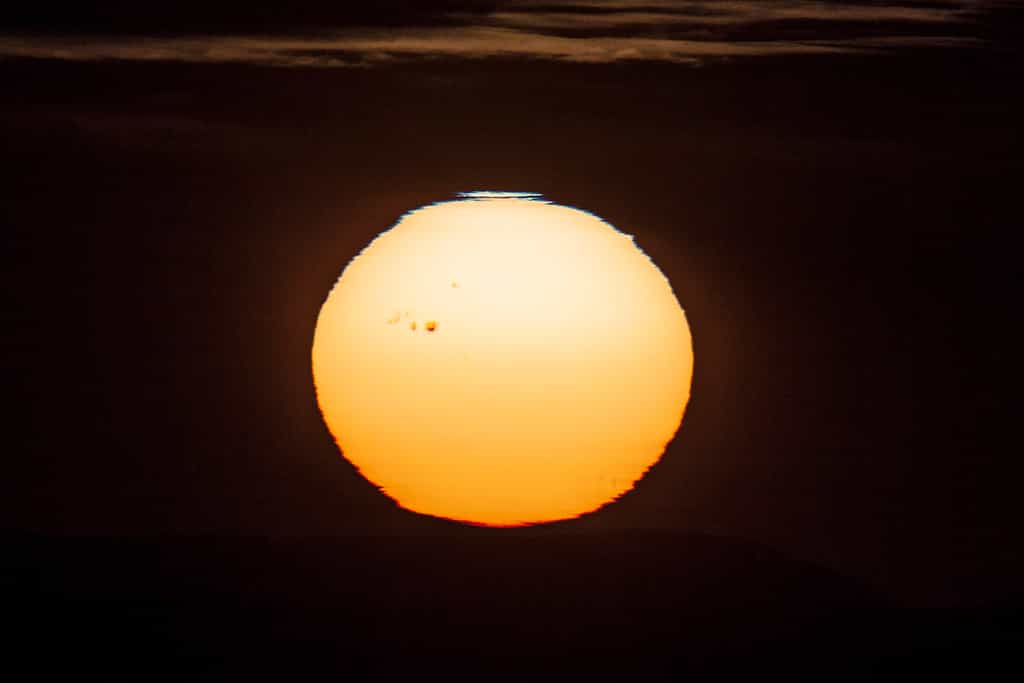 Un immense groupe de taches sombres macule la surface du Soleil, photographiée lors du coucher de l'astre du jour. Attention, il ne faut jamais regarder directement le Soleil sans protection adaptée. © Jürg Alean