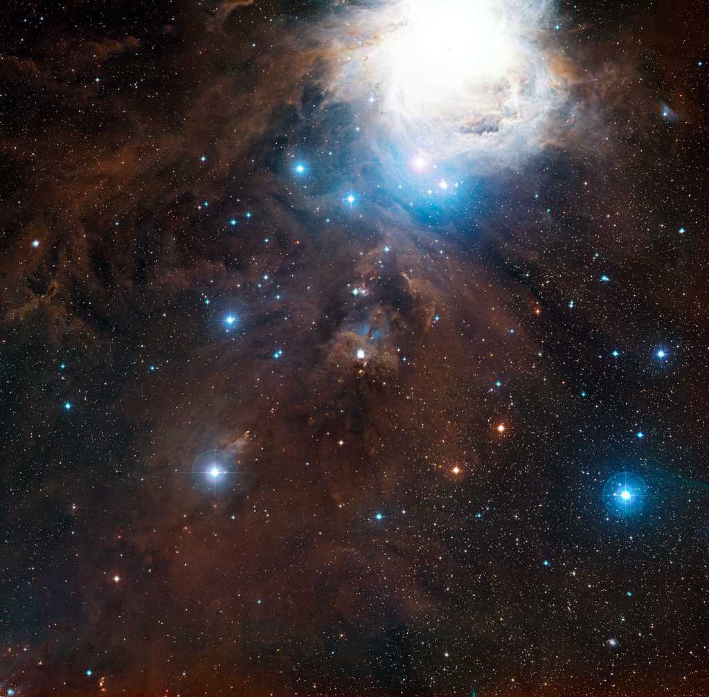 Cette image à grand champ montre la région autour de la nébuleuse par réflexion NGC 1999 dans la fameuse constellation d’Orion en lumière visible. NGC 1999 se trouve au centre de l’image. La grande structure brillante en haut de l’image est la nébuleuse bien connue d’Orion (Messier 42). Cette vue a été créée à partir de clichés du&nbsp;Digitized Sky Survey 2. © ESO,&nbsp;Digitized Sky Survey 2, Davide De Martin