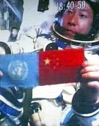 Dans son vaisseau en orbite autour de la Terre, Yang Liwei brandit le drapeau des Nations Unies et le drapeau chinois.