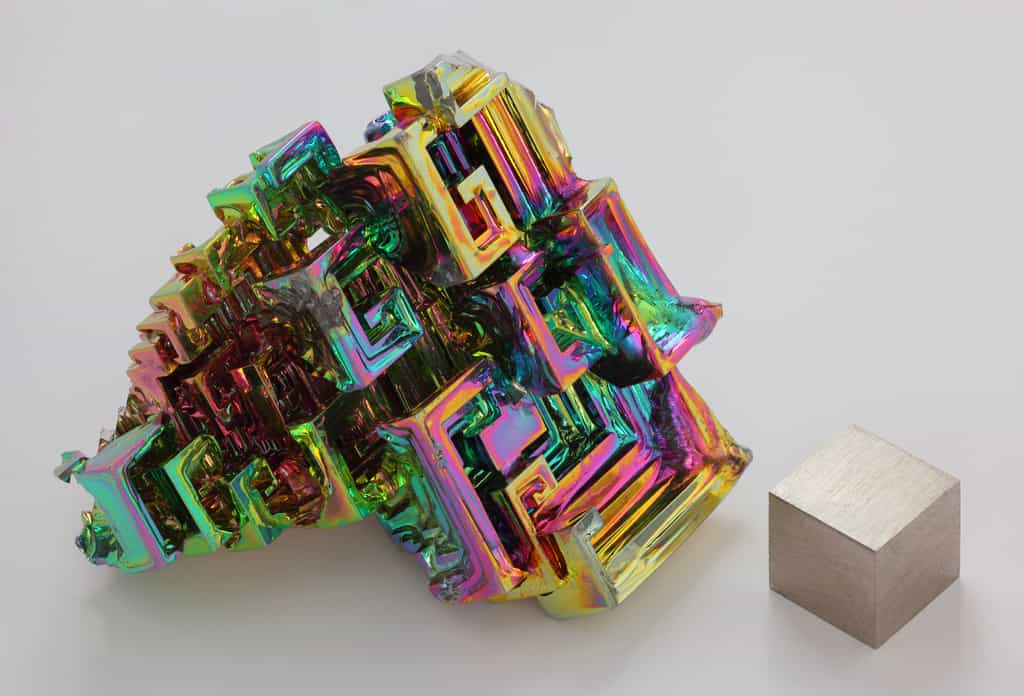 Cristal obtenu par cristallogenèse artificielle de bismuth métallique à coté d'un cube d'1 cm3 de bismuth pur à 99,99 %. L'irisation est due à une couche d'oxyde très mince. © Alchemist-hp, Wikiemdia Commons, CC by-nc-nd 3.0