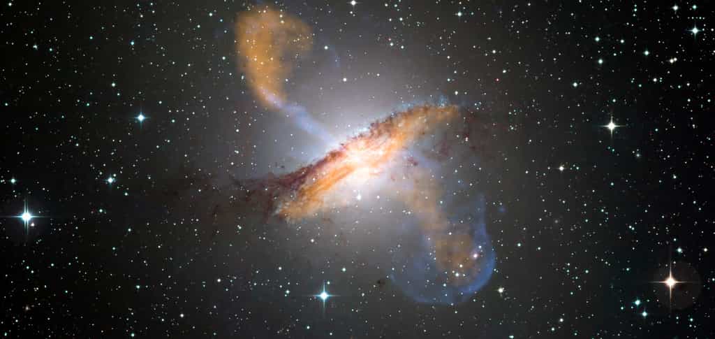 Une image en couleurs de Centaurus A, révélant les jets émis par le très actif trou noir central de la galaxie. Ceci est une image composite obtenue avec trois instruments différents fonctionnant à différentes longueurs d'onde. Les données à 870 micromètres, de Laboc, sur Apex, sont montrées en orange. Les données aux rayons X, de l'observatoire de Chandra, sont montrées en bleu. Les données de la lumière visible, du Wide Field Imager (WFI) du télescope MGP/ESO de 2,2 mètres, situé à La Silla (Chili), montre les étoiles. La ligne de poussière caractéristique de la galaxie est proche des « couleurs réelles ». © ESO/WFI (Optical) ; MPIfR/ESO/APEX/A.Weiss et al. (Submillimetre) ; NASA/CXC/CfA/R.Kraft et al. (X-ray)