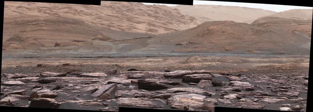 Extrait d’une vue panoramique créée à partir d'images pris la caméra du mât de Curiosity lors du Sol 1520. Les teintes pourpres des roches au premier-plan indiquent la présence d’hématite. À l'arrière-plan, les collines contenant davantage&nbsp;sulfates sont la&nbsp;prochaine destination du rover. © Nasa, JPL-Caltech, MSSS