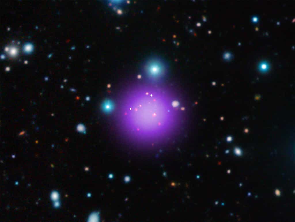 Les amas de galaxies tels que CL J1001+0220, qui est donc l'amas le plus lointain connu, constituent les plus grandes accumulations de matière soudées par la gravitation qui sont nées depuis le Big Bang. Selon le scénario accepté de formation hiérarchique des structures, ces amas se seraient formés en dernier, après les étoiles puis les galaxies. L’image montre en violet l’émission de rayons X, captée par le satellite Chandra. Ceux-ci sont issus de la matière située entre les galaxies et qui est chauffée à plusieurs millions de degrés par l’énorme gravité de l’amas. © X-ray : NASA/CXC/Université Paris/T.Wang et al ; Infrared : ESO/UltraVISTA ; Radio : ESO/NAOJ/NRAO/ALMA