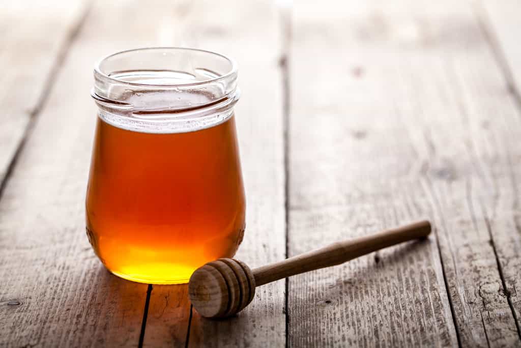 Un pot de miel posé sur une table avec une cuillère en bois ©serbogachuk