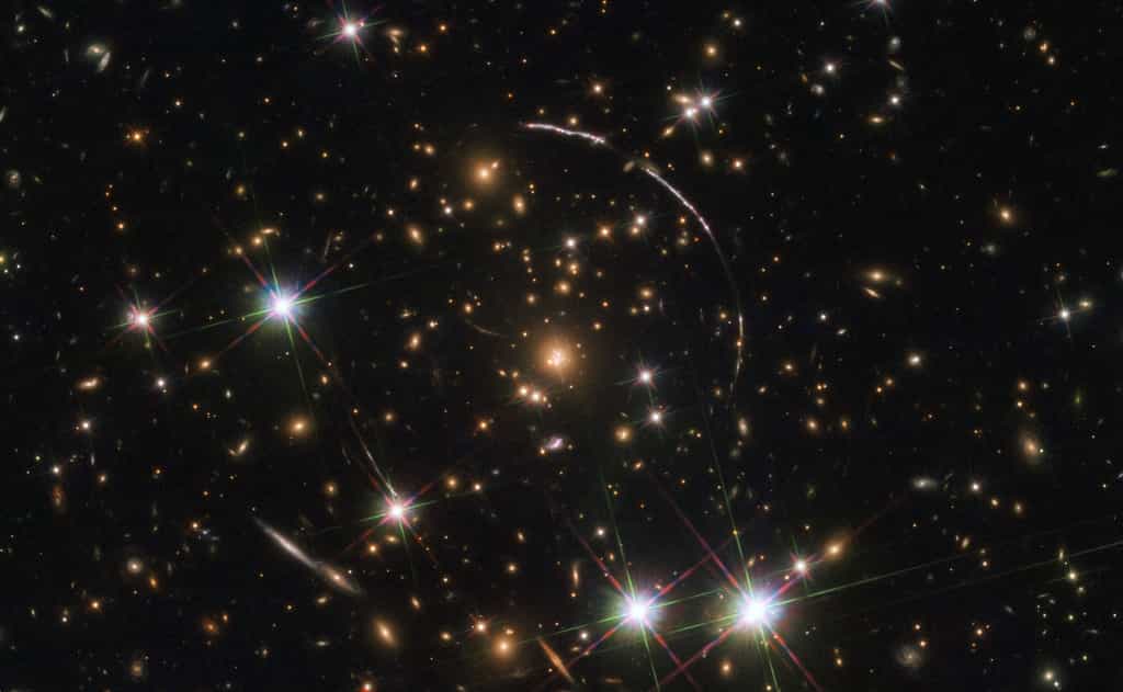 Cette image, prise avec le télescope spatial Hubble Nasa-ESA, montre un gigantesque amas de galaxies situé à environ 4,6 milliards d'années-lumière. Le long de ses frontières, quatre arcs lumineux sont visibles. Ce sont des copies de la même galaxie lointaine surnommée Arc Sunburst. La galaxie Sunburst Arc est à près de 11 milliards d’années-lumière. Trois arcs sont visibles en haut à droite de l'image, le quatrième en bas à gauche. Le dernier est partiellement masqué par une étoile brillante au premier plan, située dans la Voie lactée. © ESA, Hubble, Nasa, Rivera-Thorsen et al.