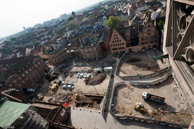 Vue panoramique des bâtiments entourant la place du Château à Strasbourg, en 2012.&nbsp;Le cliché est pris depuis la cathédrale, vers le sud. Au premier plan, l'opération archéologique ; à l'arrière-plan, sur la gauche, l'avancée d'un suivi de réseau. © Inrap