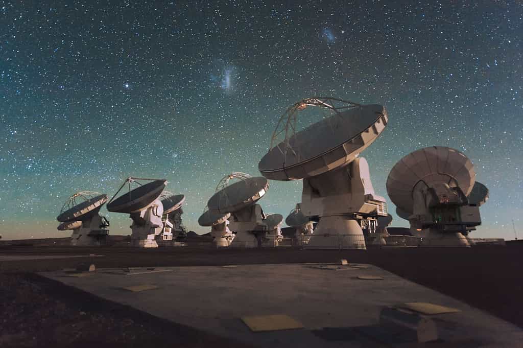 Les deux nuages de Magellan visibles au-dessus d’une partie du Vaste Réseau (Sub-) Millimétrique de l’Atacama, Alma. « À l’avenir, Alma produira des images de la structure fine des galaxies primordiales et retracera le détail de la formation des toutes premières galaxies » explique Roberto Maiolino qui a contribué à cette étude qui a permis de mieux cerner des galaxies très jeunes et lointaines. © Eso, C. Malin