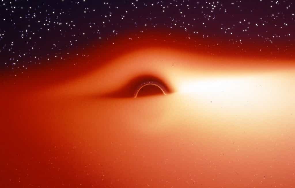 Le champ de gravitation d'un trou noir déforme fortement l'image du disque d'accrétion qui l'entoure et qui contient un plasma chaud et lumineux en rotation autour de l'astre. On peut s'en rendre compte avec cette image, extraite d'une simulation de ce que verrait un observateur s'approchant de l'astre compact selon une direction légèrement inclinée au-dessus du disque d'accrétion. La partie du disque située derrière le trou noir semble tordue à 90° et devient visible au-dessus du trou noir. Du fait du décalage Doppler, le disque d'accrétion est plus lumineux d'un côté que de l'autre. Jean-Pierre Luminet a fait la première simulation de ces images en 1979, bien avant celle montrée dans Interstellar qui contient, fiction oblige, quelques simplifications trompeuses. © Jean-Pierre Luminet, Jean-Alain Marck