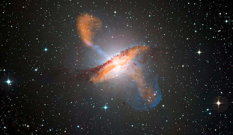 Une image de Centaurus A révélant les jets émis par le très actif trou noir central de cette galaxie, réalisée avec trois instruments fonctionnant à différentes longueurs d'onde. Les données submillimétriques à 870 microns obtenues à l'aide du télescope Apex et la caméra Laboca (<em>Large Apex Bolometer Camera</em>) sont figurées en orange. Les données en rayons X de Chandra sont montrées en bleu. Les données de lumière visible du WFI (<em>Wide Field Imager</em>) du télescope MPG-Eso de 2,2 mètres situé à La Silla, au Chili, montrent les étoiles et la ligne de poussières caractéristique de la galaxie quasiment en couleurs réelles. © Eso, Nasa