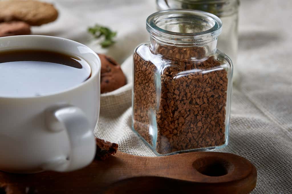 Un pot de café soluble à côté d'une tasse de café. © Aleksey, Adobe Stock