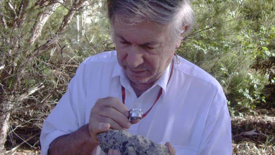 Andrew Glikson examine un échantillon de suévite, une roche formée par l'impact d'une météorite sur Terre. Il s'agit d'une brèche d'impact présentant des fragments de roche liés dans une matrice. © D. Seymour 