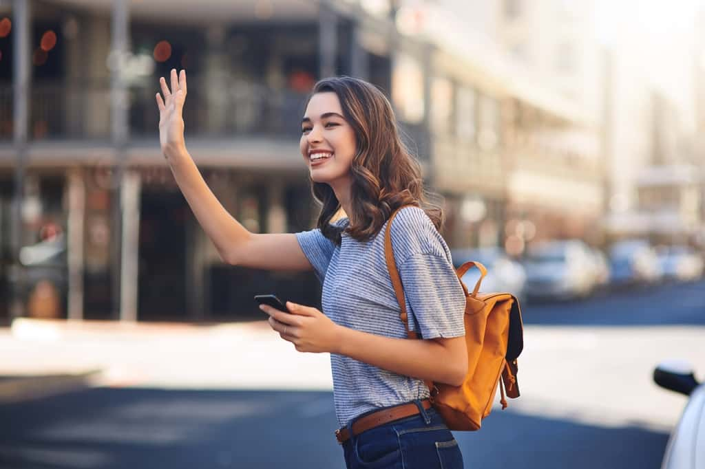 Une jeune femme téléphone en main fait signe pour être prise dans un véhicule © JordaanExams/peopleimages.com, Adobe Stock