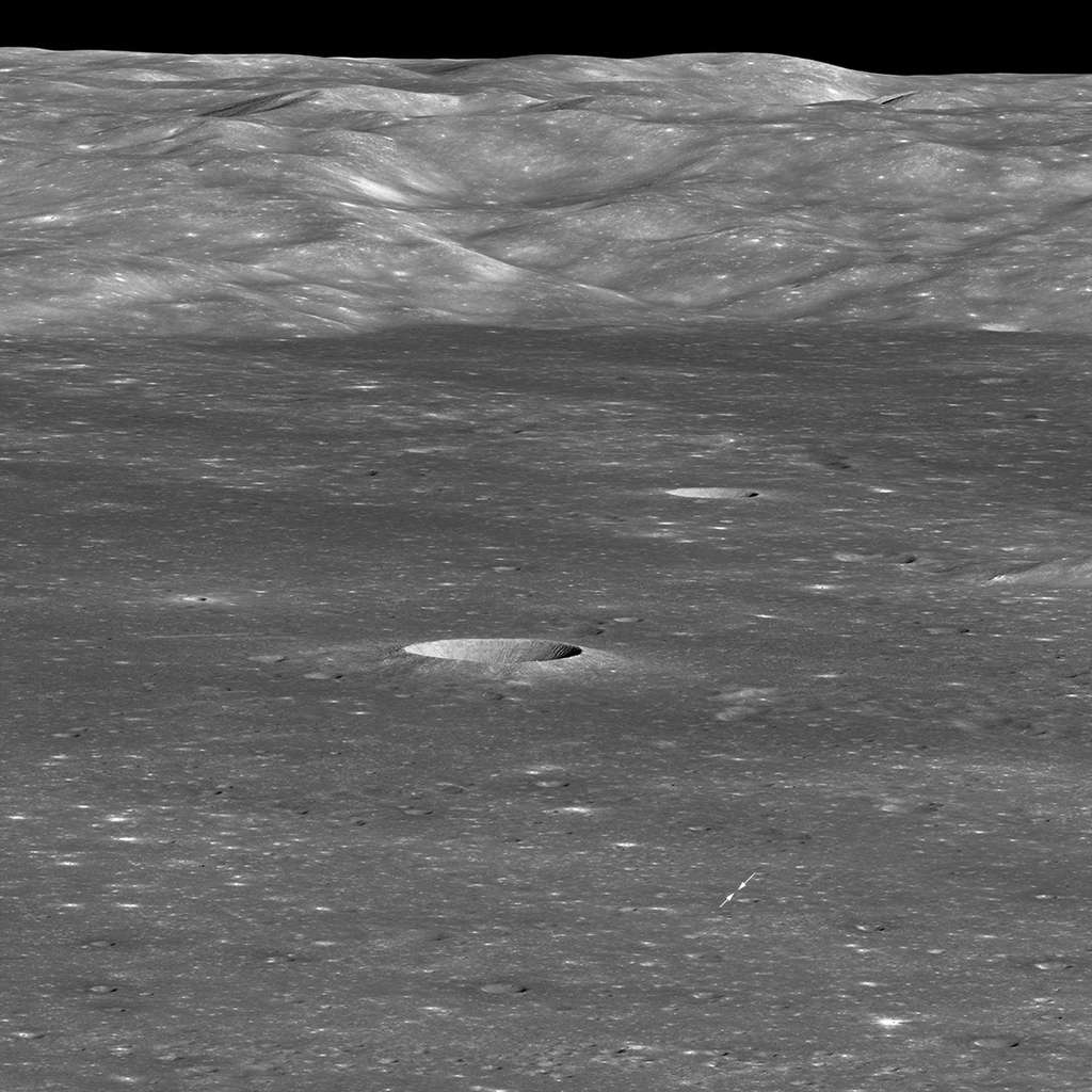 Le cratère von Kármán, terrain de jeu lunaire de la mission chinoise Chang'e 4, vu par la sonde spatiale américaine LRO en orbite autour de la Lune le 30 janvier 2019. L'atterrisseur est le tout petit point blanc indiqué par les deux flèches. Le rover Yutu 2 n'est pas visible. Les montagnes au loin forment la paroi occidentale du cratère von Kármán. Le petit cratère que l'on voit très clairement au milieu de l'image fait 3.900 m de diamètre et 600 m de profondeur. © Nasa/GSFC/<em>Arizona State University</em>