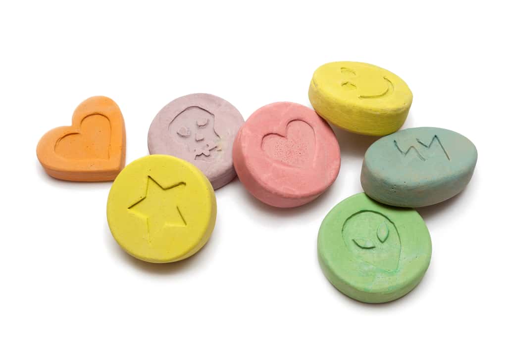 L'ecstasy est une drogue psychoactive qui se présente sous forme de petites pilules colorées. Les effets comprennent des hallucinations, une énergie accrue, de l'empathie et du plaisir. © portokalis, Adobe Stock