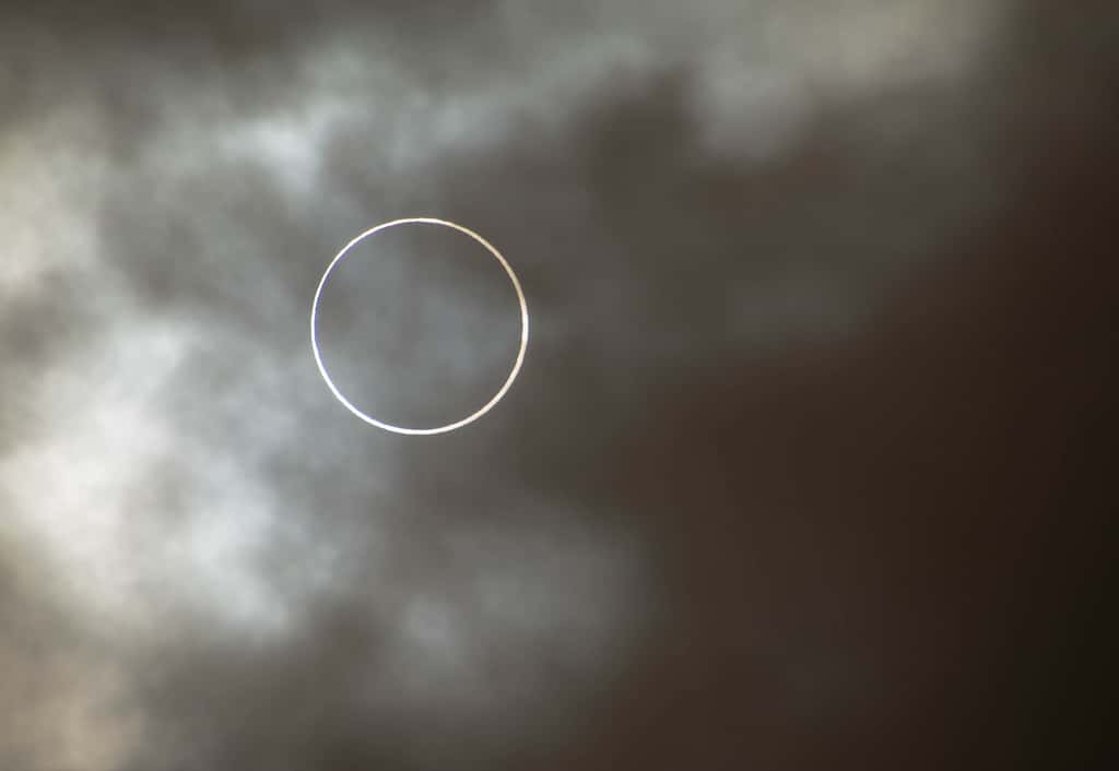 Menaçant, le voile nuageux ne fut pas assez épais pour occulter l’éclipse annulaire du Soleil à la Réunion. Le disque lunaire est quasiment centré sur celui de l’astre du jour. On peut distinguer les aspérités du relief sur le limbe de notre satellite. © Dave Pot, Flickr