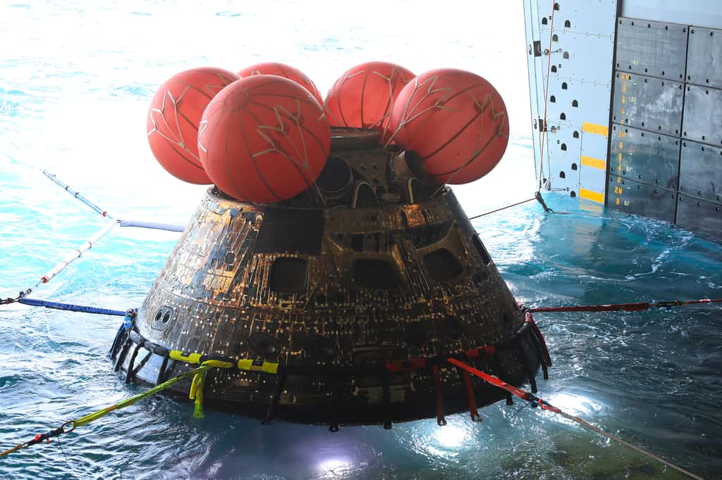 La capsule Orion, débarrassée de son module de service, est montée à bord de l'USS Portland qui va la ramener à San Diego d'où elle sera acheminée au Centre Spatial Kennedy. Comme on peut le constater visuellement, la traversée de l'atmosphère à très haute température a laissé quelques traces ! Près de 2 800 °C tout de même. © Nasa