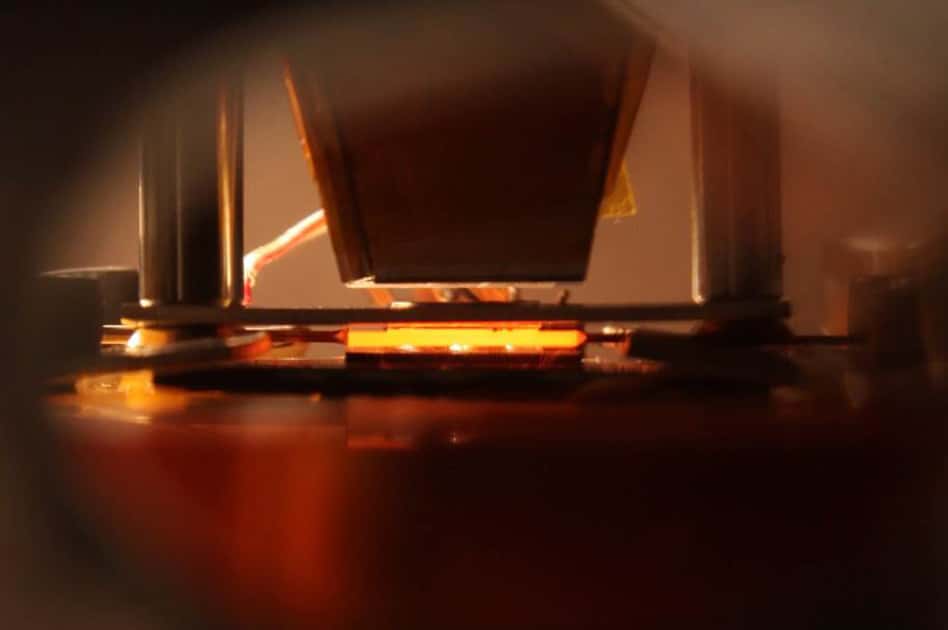 Dans cette image, l’absorbeur-émetteur imaginé au MIT est en plein fonctionnement. Il s’agit de la structure orange qui brille au centre de l’image, au-dessus de la cellule photovoltaïque. Notons que les tests ont été réalisés dans un environnement sous vide. © John Freidah