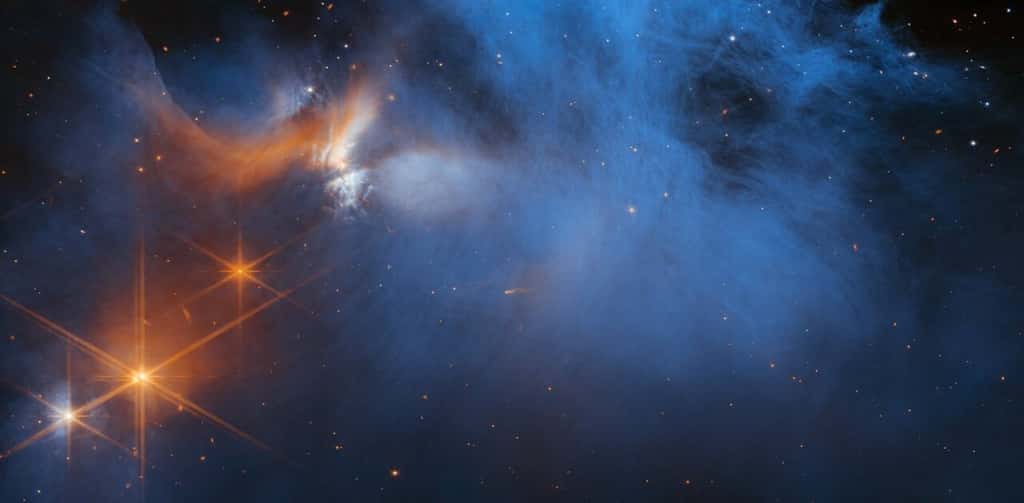Cette image de la caméra proche infrarouge (NIRCam) du télescope spatial James-Webb de la Nasa/ESA/CSA présente la région centrale du nuage moléculaire sombre Caméléon I, qui se trouve à 630 années-lumière du Soleil. Le matériau nuageux froid et vaporeux (bleu, au centre) est illuminé dans l'infrarouge par la lueur de la jeune protoétoile Ced 110 IRS 4 (orange, en haut à gauche). La lumière de nombreuses étoiles d'arrière-plan, vues comme des points orange derrière le nuage, peut être utilisée pour détecter les glaces dans le nuage, qui absorbent la lumière des étoiles qui les traverse. © Nasa, ESA, CSA, and M. Zamani (ESA/Webb); Science: F. Sun (Steward Observatory), Z. Smith (Open University), and the Ice Age ERS Team