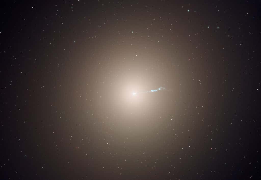 La galaxie elliptique M87 abrite plusieurs milliers de milliards d'étoiles, un trou noir supermassif et une famille d'environ 15.000 amas globulaires. À titre de comparaison, notre galaxie de la Voie lactée ne contient que quelques centaines de milliards d'étoiles et environ 150 amas globulaires. Cette image de M87 en fausses couleurs est en réalité composite et a été formée à partir d'observations de Hubble en lumière visible et infrarouge. On voit clairement un jet de matière que l'on sait associé au trou noir M87* imagé en 2019 par les membres de l'<em>Event Horizon Telescope</em>. © <em>Nasa, ESA and the Hubble Heritage Team (STScI/AURA); P. Cote (Herzberg Institute of Astrophysics) E. Baltz (Stanford University)</em>
