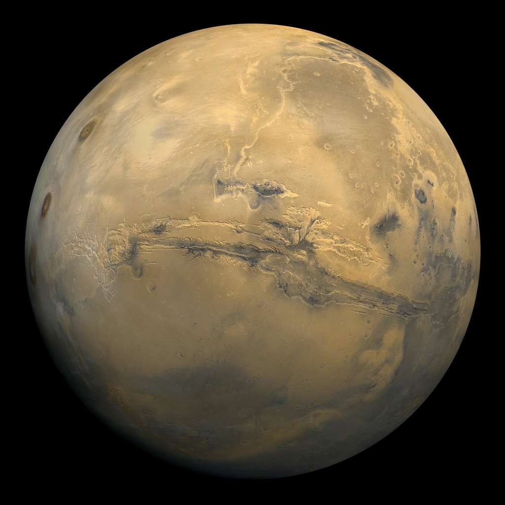 Cette mosaïque globale de 102 images de Mars prises par Viking 1 Orbiter en orbite autour de Mars, le 22 février 1980 montre <em>Valles Marineris</em> déchirant l'est du renflement de <em>Tharsis</em> avec, au centre, les plateaux de Syria, Solis et Thaumasia et, à l'ouest, les trois volcans de <em>Tharsis Montes</em>. Les images sont projetées en perspective ponctuelle, représentant ce qu'un observateur verrait depuis un vaisseau spatial à une altitude de 2 500 km. Au centre, se trouve <em>Valles Marineris</em>, long de plus de 3 000 km et profond de 8 km. Notez les canaux qui remontent (au nord) depuis les parties centrale et orientale de <em>Valles Marineris</em> jusqu'à la zone sombre, <em>Acidalic Planitia</em>, en haut à droite. © Nasa