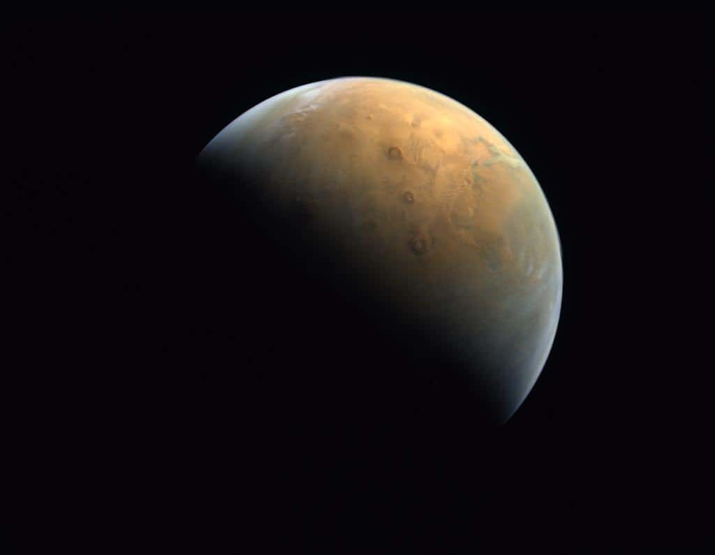 Première photo de Mars prise par la sonde Hope à 25.000 kilomètres au-dessus de la surface de la planète rouge. On distingue les trois volcans alignés des monts Tharsis. © MRSBC