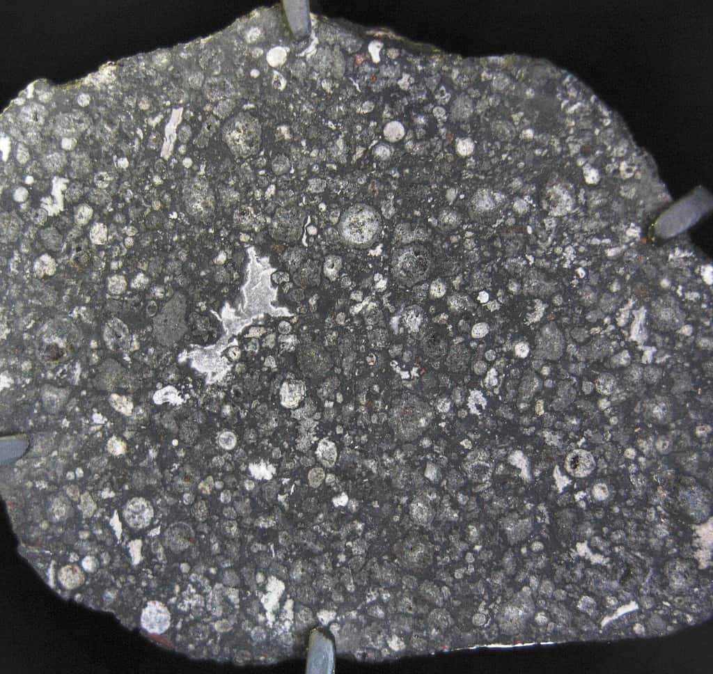 Une coupe de la célèbre météorite Allende. Cette chondrite carbonée contient des structures irrégulières blanchâtres, des CAI (pour <em>Calcium-Aluminum-rich Inclusions,</em> en anglais). Leur formation date de 4,568 milliards d'années et elles contiennent des traces de radioactivités éteintes. © CC by 20, Shiny Things