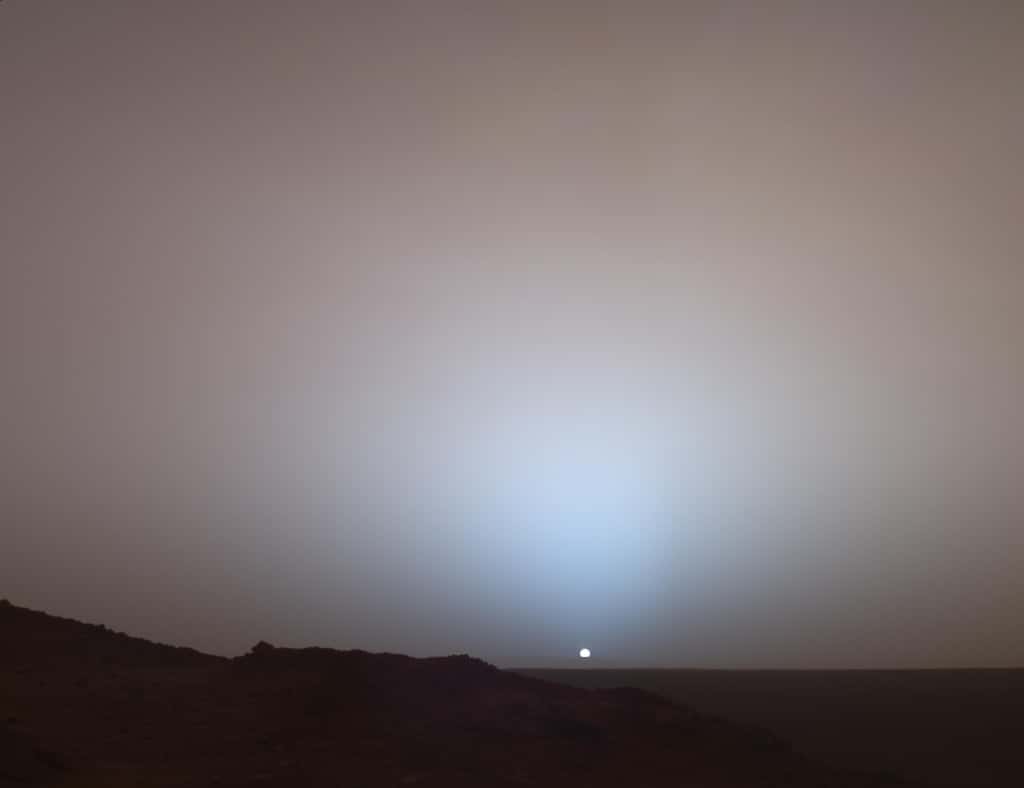 Magnifique coucher de Soleil photographié sur Mars par Spirit le 19 mai 2005 (489<sup>e</sup> sol). On distingue, à l'horizon, les « remparts » du cratère Gusev, distant de 80 kilomètres du rover. Sur Mars, le Soleil apparaît un tiers plus petit que depuis la Terre. © Nasa, JPL-Caltech, <em>Texas A &amp; M</em>, université Cornell