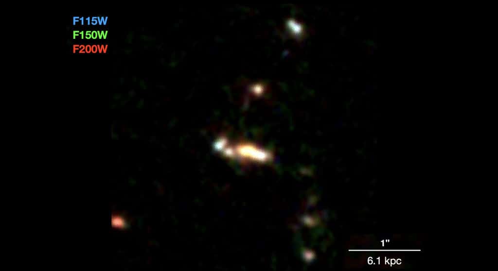 Le groupe de petites galaxies CGG-z5, vu il y a près de 13 milliards d’années, probablement en train de former une galaxie massive. Les couleurs sont composées de trois couleurs infrarouges différentes. La barre horizontale blanche montre l’échelle d’environ 20 000 années-lumière. © Shuowen Jin et <em>al.</em>, Université de Copenhague