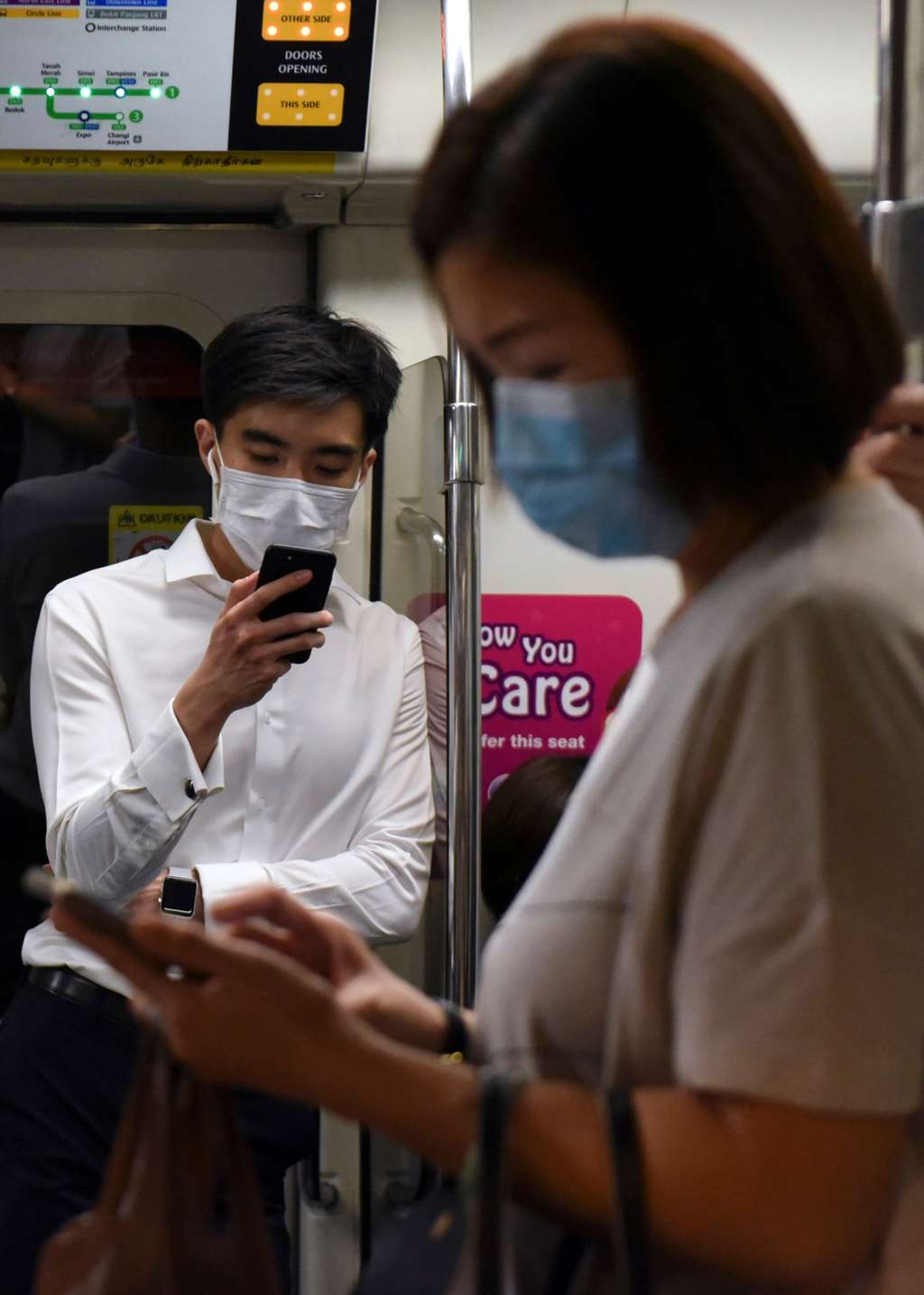 Des banlieusards portant des masques facial et regardent leurs téléphones portables dans le Métro du Singapour, le 18 mars 2020. © Catherine Lai, AFP 