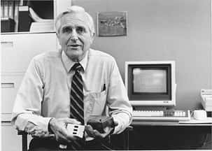 En 1968, Douglas Engelbart présente son prototype de souris (dans sa main gauche) et un modèle à trois boutons (dans sa main droite). © SRI